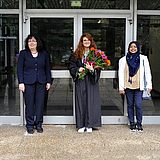 Eine Person mit Blumen in der Hand steht neben anderen vor einem Eingang